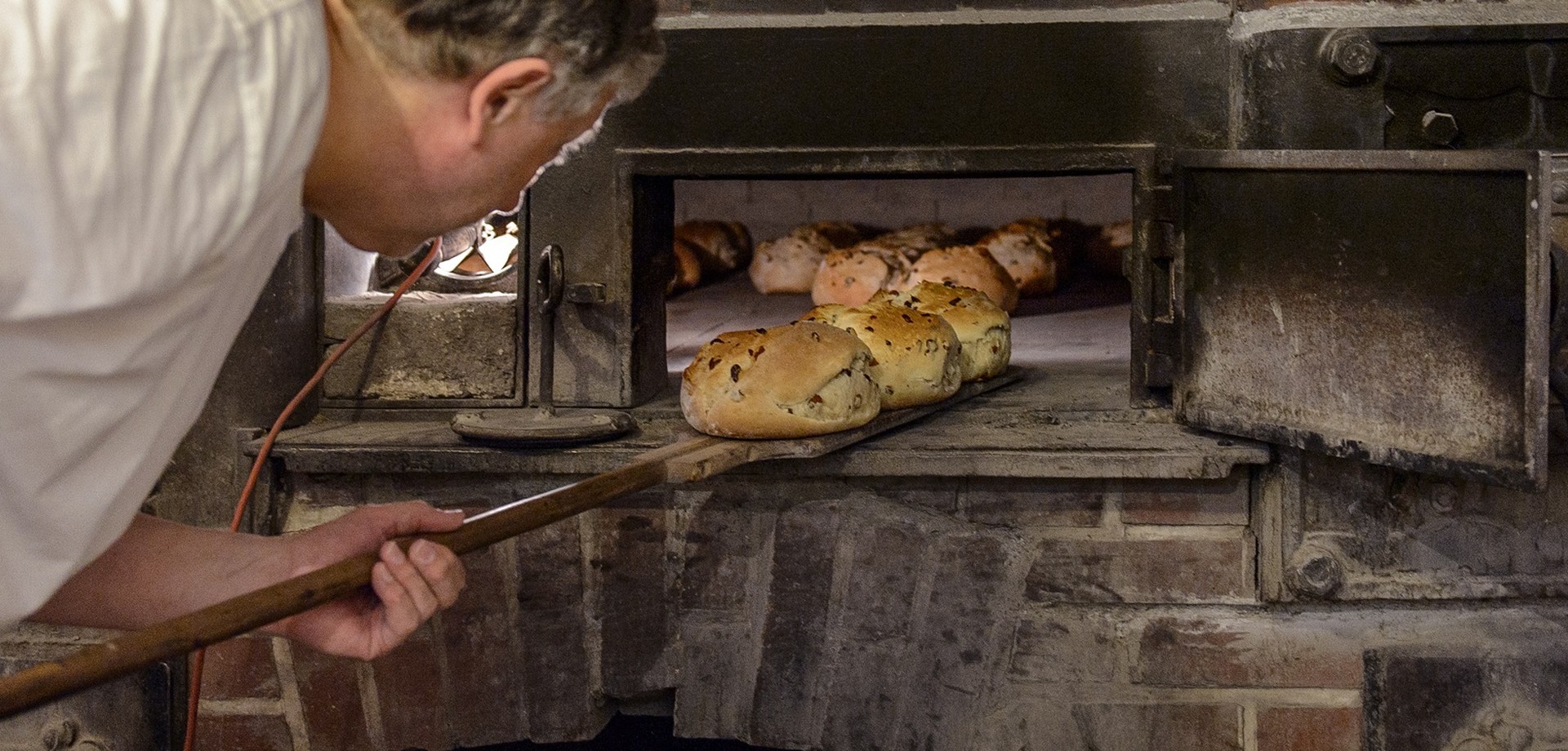 Ein Bäcker holt große Rosinenbrötchen aus einem alten Steinofen