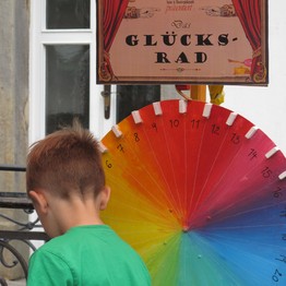 Ein Kind mit einem grünen T-Shirt steht vor einem bunten Glücksrad
