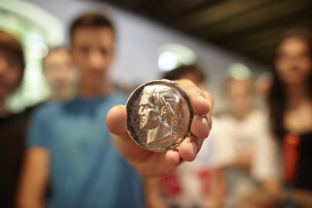 Ein junger Mann hält eine Münze in die Kamera