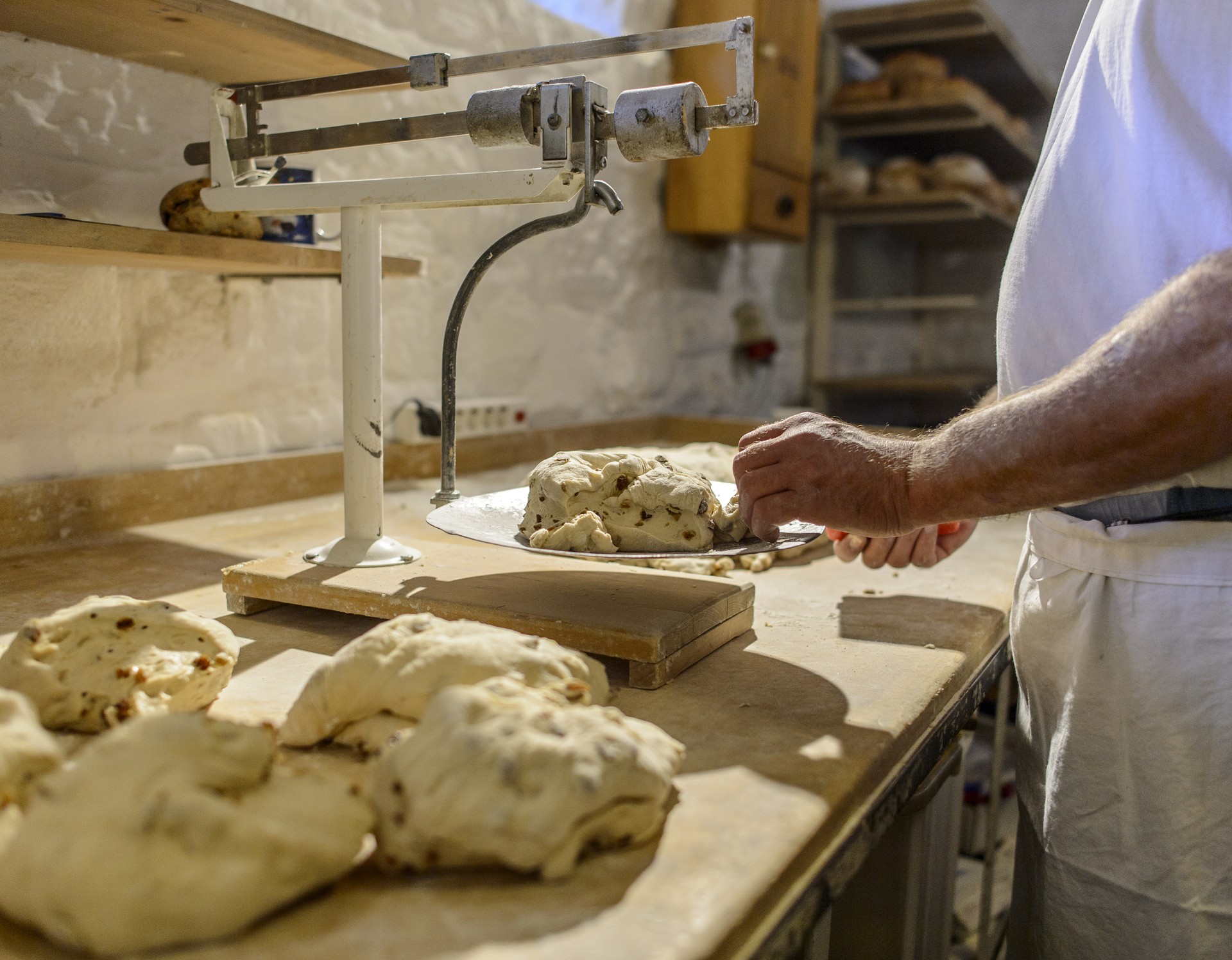 Ein Bäcker wiegt Teig für Rosinenstuten auf einer altmodischen Waage ab