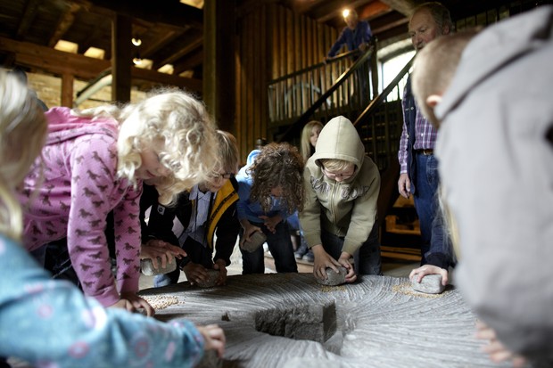 Kinder mahlen Mehl auf einem großen Mühlstein