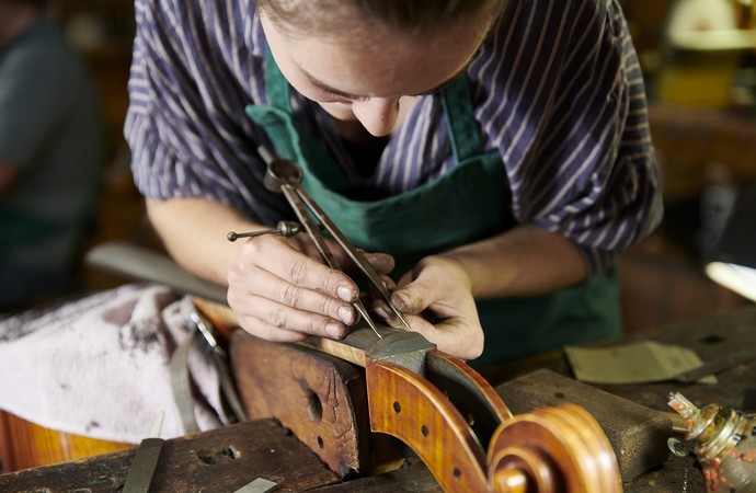 Eine Frau beugt sich über eine Geige und arbeitet an ihr