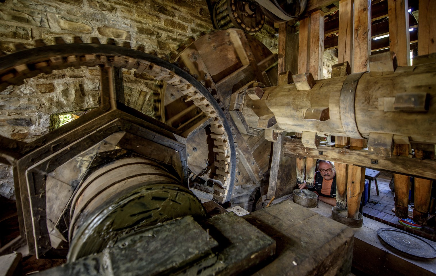 rechts unten im Bild schaut ein Mann durch große hölzerne Zahnräder