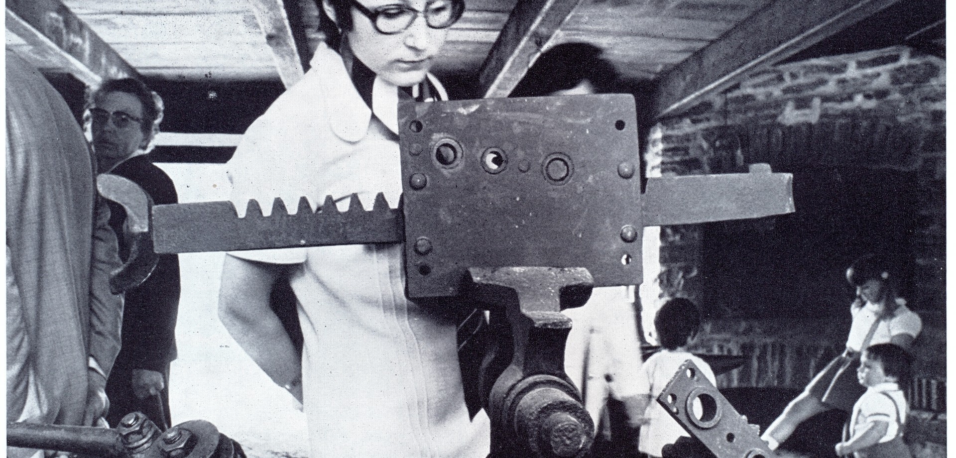 Ein Foto aus den 70er Jahre. Eine Frau betrachtet eine Maschine in einer Werkstatt.