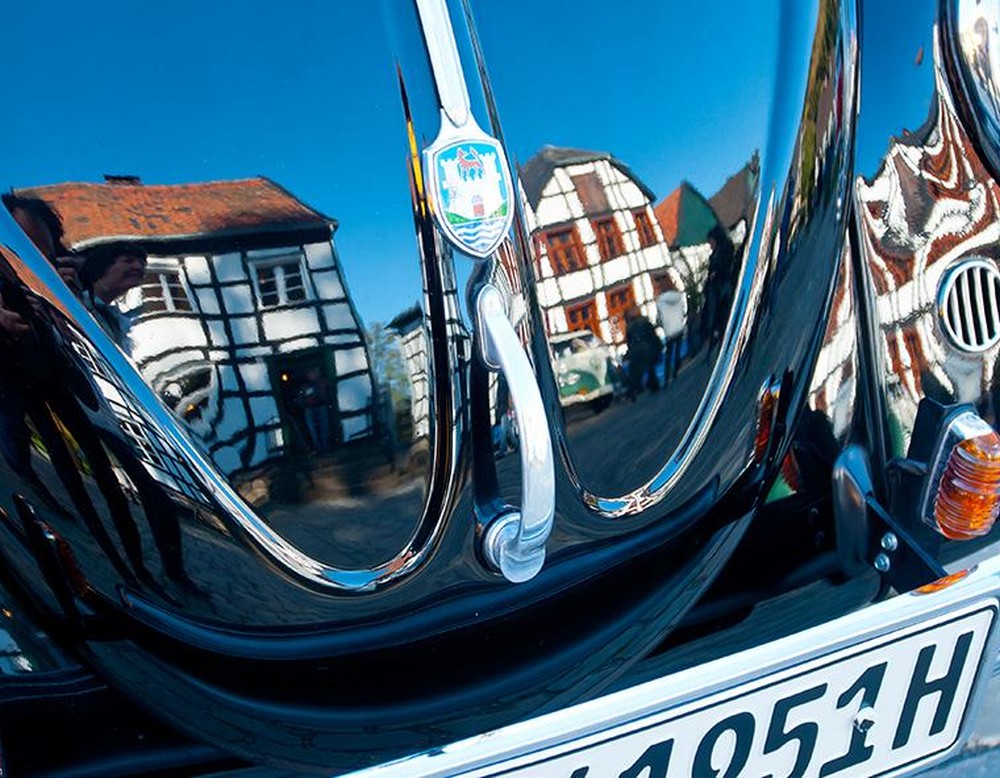 Das Bild zeigt eine Motorhaube in der sich Fachwerkhäuser spiegeln