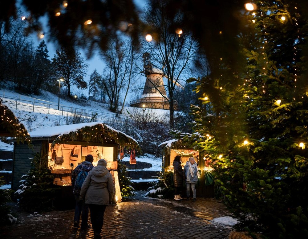 Beleuchtete Weihnachtsmarkthütten mit einer Windmühle im Hintergrund.